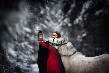 A girl in a winter forest. A girl and a pony. A girl in red and a white pony.