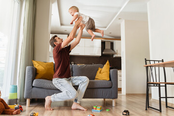 Father throwing cheerful little blond boy high in air while playing together at living room on...