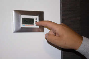 Image of the hand of a man who lowers the temperature of the house thermostat with his finger....