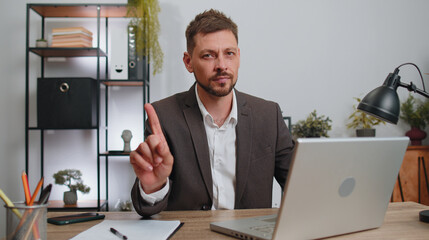 Businessman in suit working on laptop computer shakes finger and saying no, be careful, scolding...