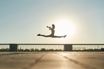 Sportswoman jumping on sunny background in city - Powered by Adobe
