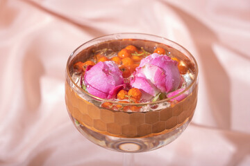 Close-up glass with beverage with mountain ash and roses on folded fabric background