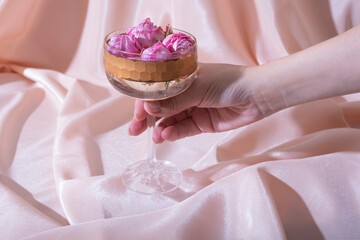 Female hand with beverage and flowers in glass on folded fabric background. Creative holiday concept.
