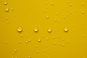 Four drops of water lined up in a row, among chaotic splashes, on a yellow surface. Abstract background. Top view. 
