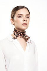 Close-up shot of a girl in a double twilly skinny scarf with an animal print. The girl in a white shirt with a twilly scarf around her neck is on a white background. Front view.