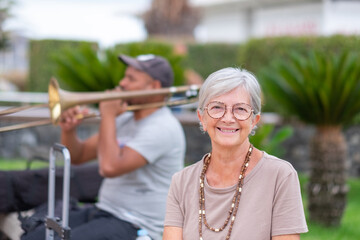 Elderly Caucasian woman sitting outdoors near a trumpet player enjoying the music