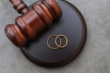 Law theme. Judge gavel wedding rings on concrete stone grey background. Divorce proceedings. Mallet...