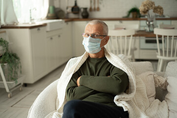 Portrait of an elderly gray-haired man in a protective face mask in a cold winter at home.