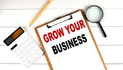 Grow your business words on clipboard, with calculator, magnifier and pencil on the white wooden background