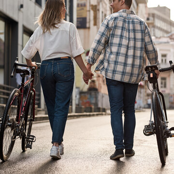Couple hold hands and walk with bicycles in city