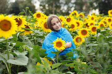 Young girl teenager wrapped in ukrainian flag in a sunflower field, horizontal