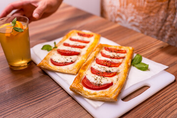 Two rectangular mini pizzas with tomatoes and mozzarella. The girl takes a glass of homemade lemonade