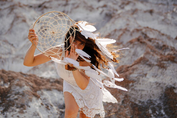 Beautiful girl in white dress holding a dreamcatcher near with her face.