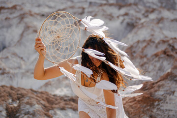 Beautiful girl in white dress holding a dreamcatcher near with her face.