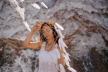 Beautiful girl in white dress holding a dreamcatcher near with her face.
