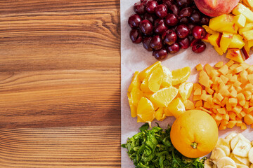 Sliced fruits and vegetables for smoothies. Orange, cherry and others. Top view, on a wooden table.