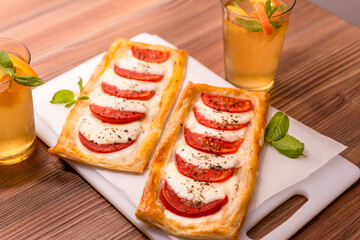 Two rectangular mini pizzas with tomatoes and mozzarella. and homemade lemonade on a wooden table.