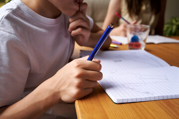 School boy drawing into exercise book, doing homework