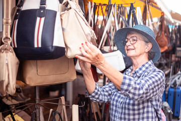 Smiling senior woman in blue hat choosing a bag in a store