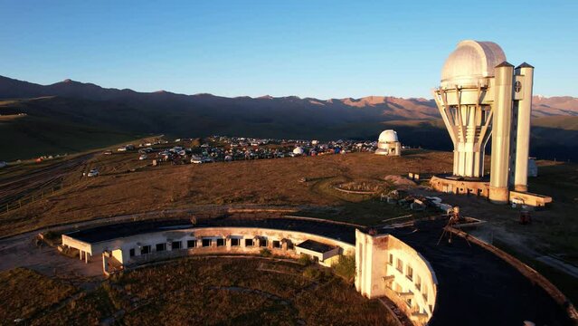 Bright dawn over the Assy-Turgen Observatory in the mountains. Aerial view from the drone of the camp of tents, cars and waking tourists. There is an old abandoned building. Kazakhstan, Almaty