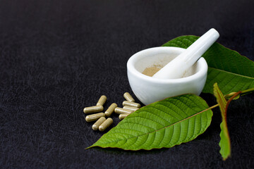 Kratom (Mitragyna speciosa) leaves and katom powder capsules on dark background.