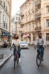 Obraz na płótnie Canvas Young couple wearing medical masks riding bikes