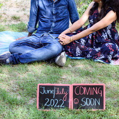 Indian couple posing for maternity baby shoot. The couple is posing in a lawn with green grass and the woman is falunting her baby bump in Lodhi Garden in New Delhi, India