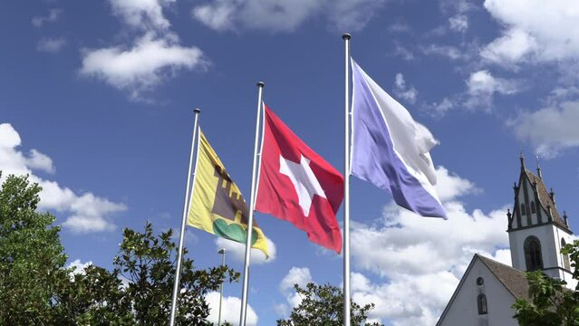 Different flags blowing in the wind, yellow and black miles flag, swiss flag and canton of zurich flag in front of blue sky, sunshine with clouds, without people