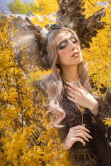 Fairy girl in a crown of feathers and long blond hair posing in yellow flowers