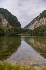 Vertical image of the two mountains reflecting from the mirror surface of the emerald turquoise Five Color Pond lake in Jiuzhaigou, Aba Tibetan Autonomous Prefecture, Sichuan, China. Cloudy sky