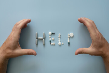 Hands laid out the word HELP from assorted pills, on a blue background. Medical concept or...