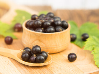 Fresh blackcurrant berries in a bowl on a wooden table near green leaves. Juicy natural currant fruits. Black currant