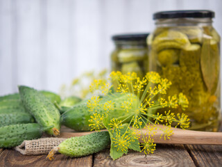 Pickled cucumbers in glass jars and fresh cucumbers and spices for making pickles on a wooden table