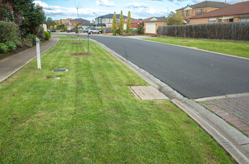 Freshly mown grass at a nature strip on a suburban road with some residential houses in the...