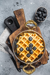 Fresh Belgian waffles with blueberry and Syrup in skillet. Gray background. Top view
