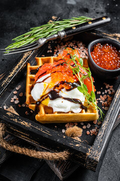 Delicious Waffle with smoked salmon fillet, poached egg and red caviar. Black background. Top view
