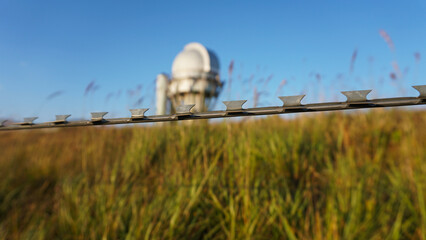 A large observatory is protected by a barbed fence. There is a long sharp wire around perimeter....