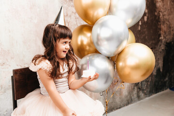 A happy little girl makes a wish and blows out the candles on the cake. balloons. Space for text....