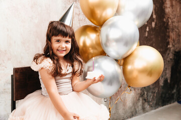 A happy little girl makes a wish and blows out the candles on the cake. balloons. Space for text....
