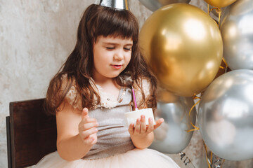 A happy little girl makes a wish and blows out the candles on the cake. balloons. Space for text....