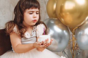 A happy little girl makes a wish and blows out the candles on the cake. balloons. Space for text....