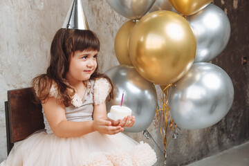 A happy little girl makes a wish and blows out the candles on the cake. balloons. Space for text....