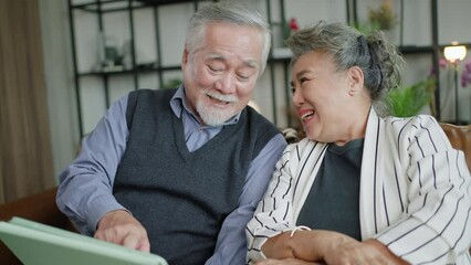 Elder asian senior couple use tablet playing game smile joyful on 5g Network technology in living room at Home,video call to their family during isolation stay home state.
 - Powered by Adobe