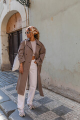 full length of stylish african american woman in headscarf and sunglasses posing with reusable bag on street in prague.