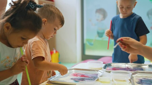 Multi-ethnic group of toddlers milk painting with the teacher helping them, using food coloring for colors. Children finger painting at the nursery school class. High quality 4k footage