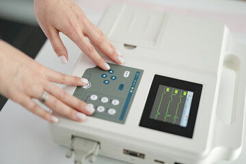 Woman cardiologist doctor makes electrocardiography procedure using cardiograph in modern clinic.