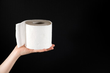 A roll of white soft toilet paper in a man's hand on a black background with space for text