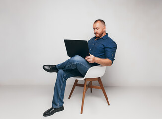 portrait of a brutal man sitting on a chair against a white wall with a laptop and notepad.a business man.