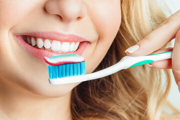 Close-up of woman brushing teeth. The girl holds a toothbrush and smiles.