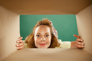 Charming young exressive girl opening, unpacking carton box and looking inside. Emotions, black...
